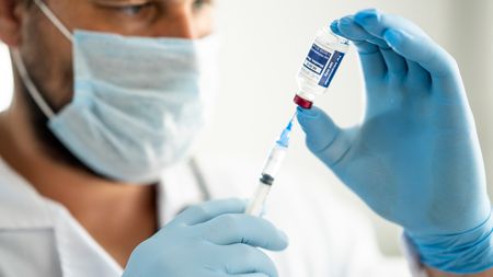 Close up of a medical professional holding a syringe drawing vaccine from a vial to prepare for injection.